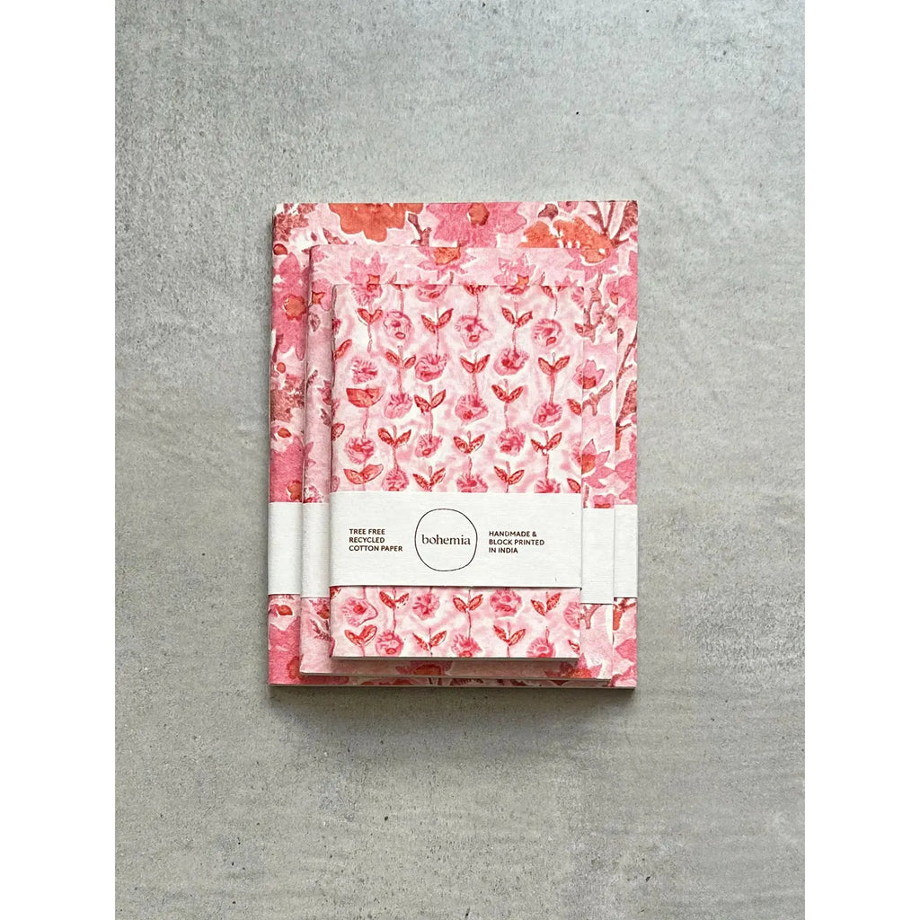 A pink floral patterned notebook with a band around it displaying the brand and details.