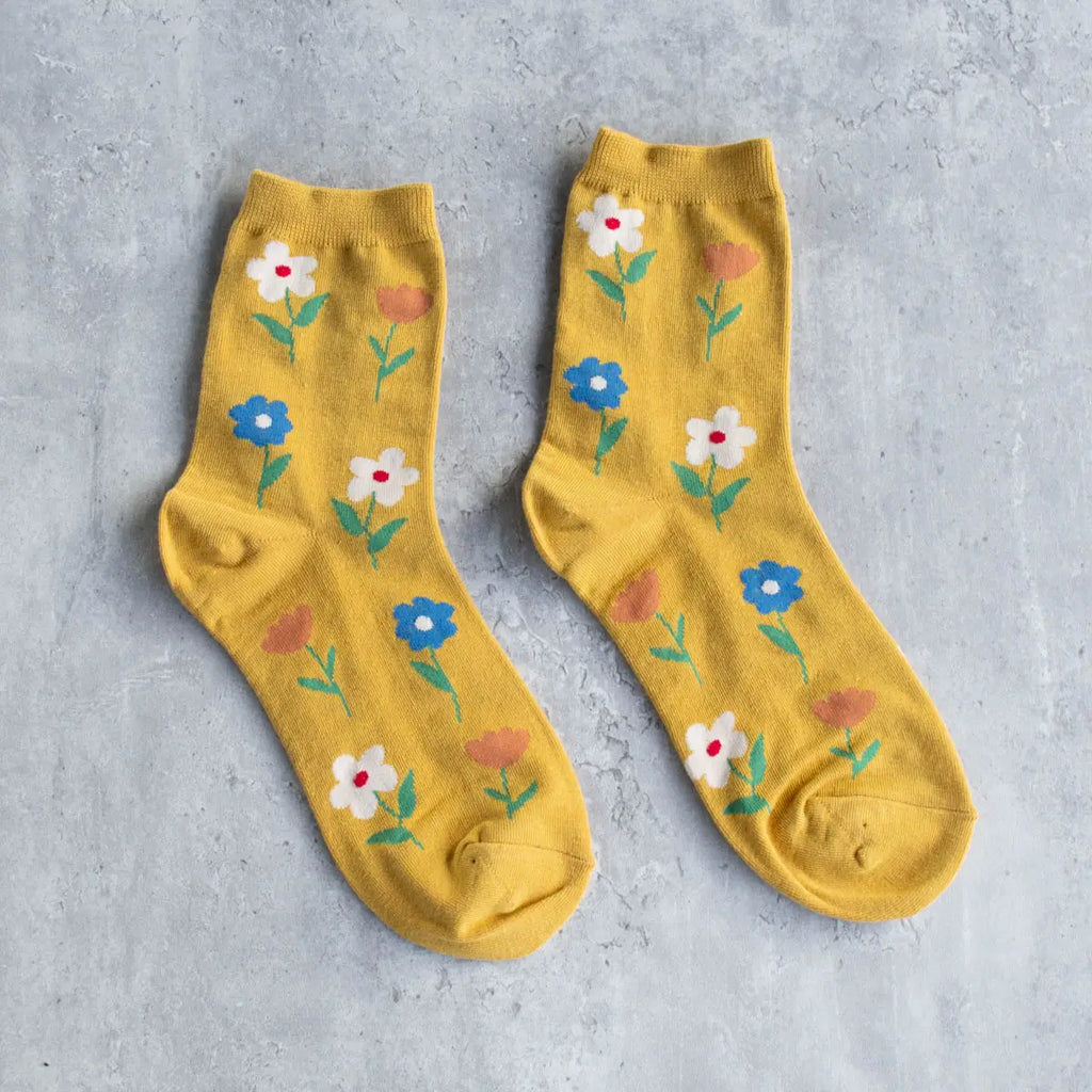 A pair of yellow socks with a floral pattern laid flat on a gray surface.