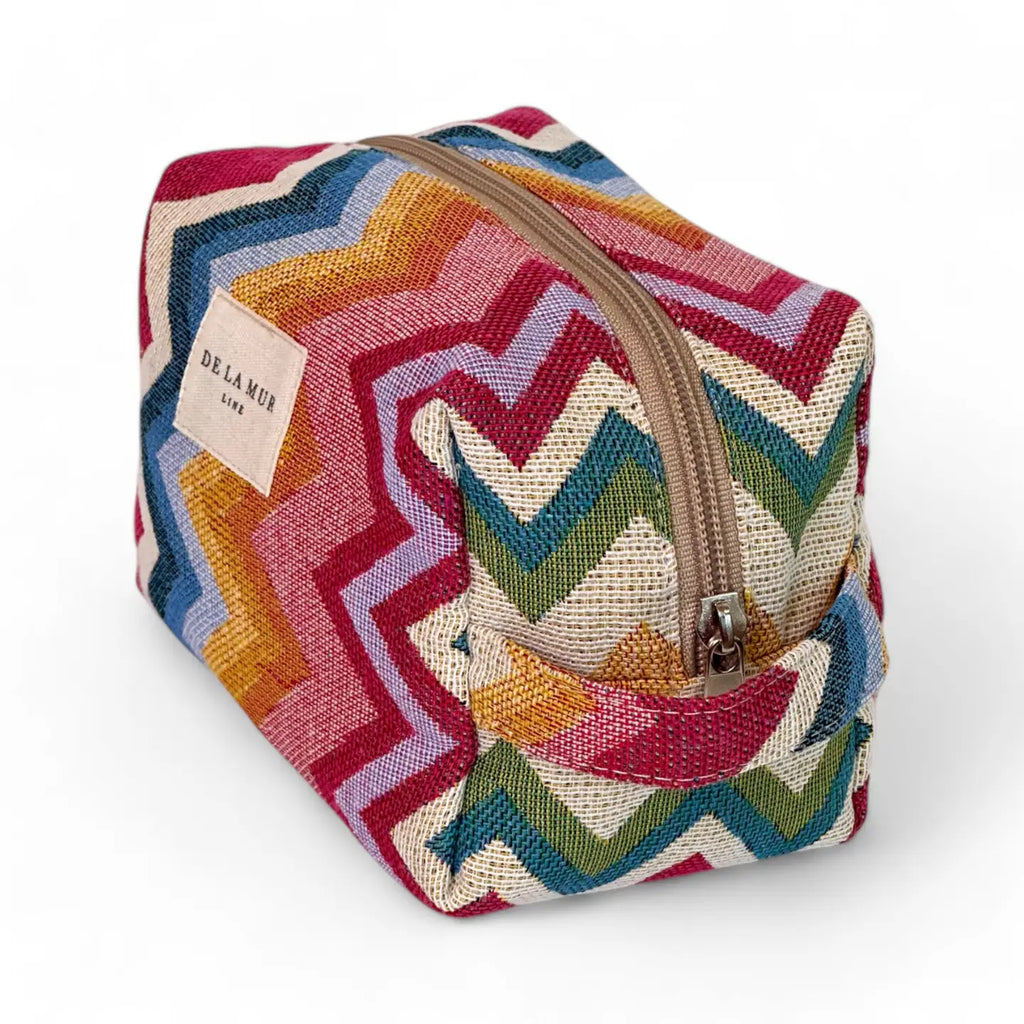 Medium toiletry bag with a zipper at the top and a side handle. Made with thick jacquard fabric with a zigzag pattern in pink and blue tones. Ideal for storing makeup, facial creams, and small bottles.
