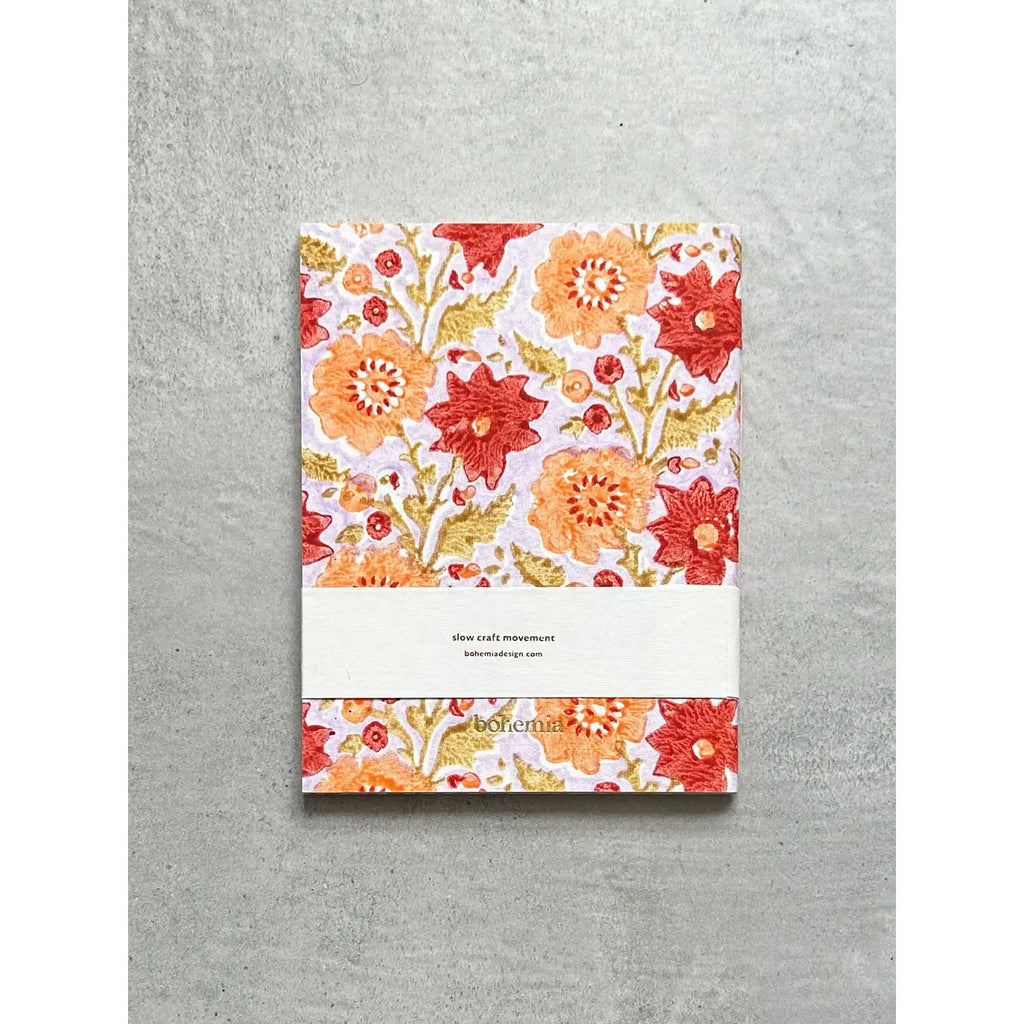 A floral patterned notebook with an elastic closure lying on a gray background.