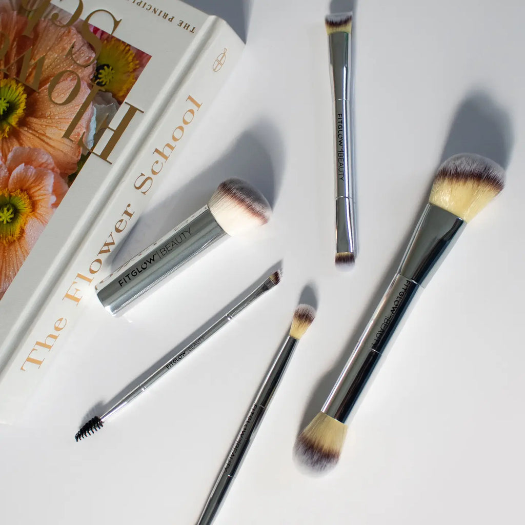 A book titled "The Flower School" placed next to the Fitglow Beauty Master Brush Set, consisting of five cruelty-free brushes of varying sizes and shapes, on a white surface.