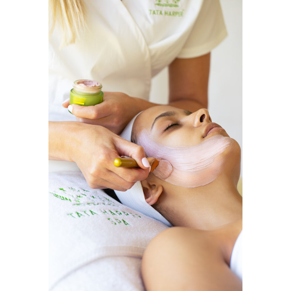 Aesthetician applying facial mask treatment to a relaxed client.