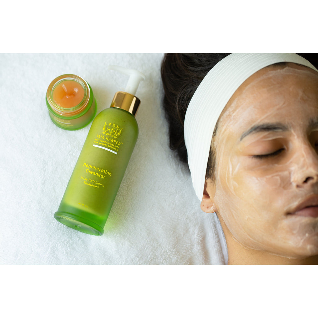 A person relaxing with a facial mask next to skincare products.