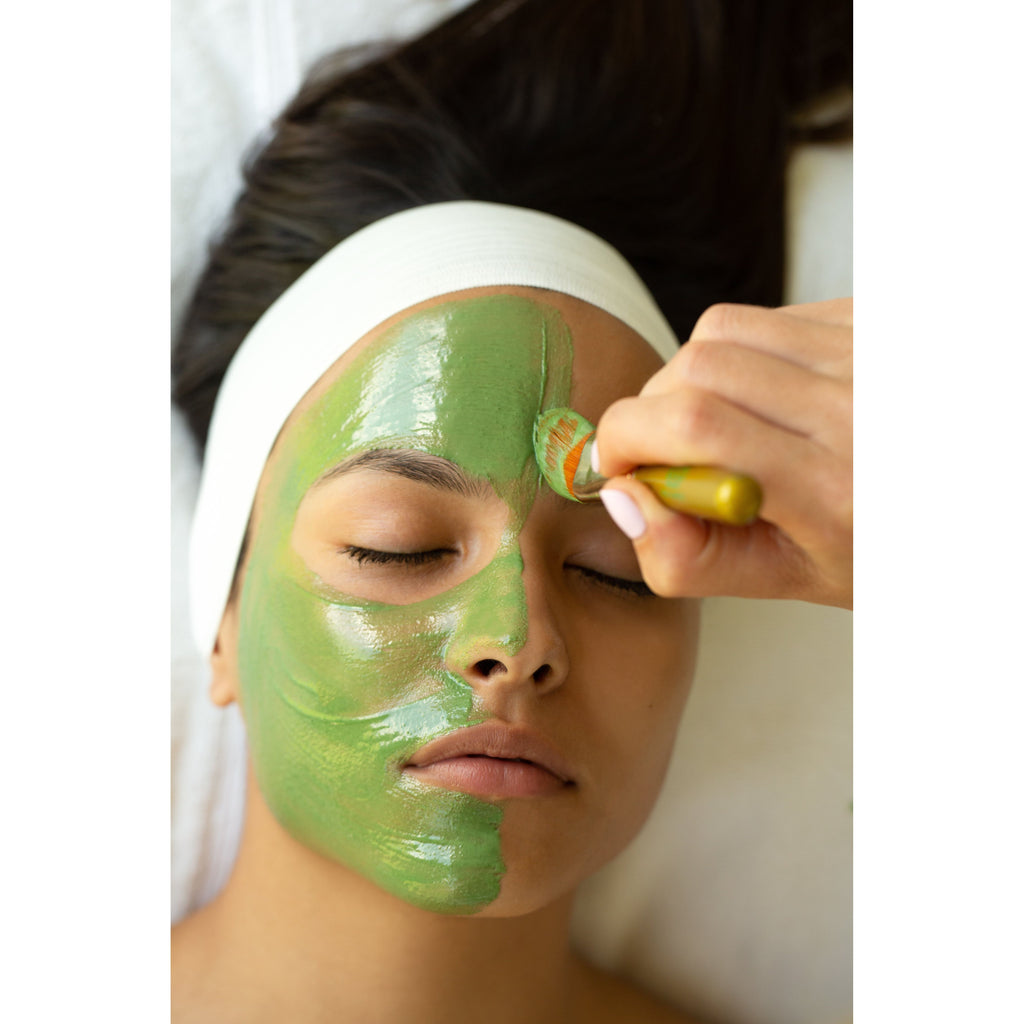 A person receiving a facial treatment with a green mask being applied to their skin.