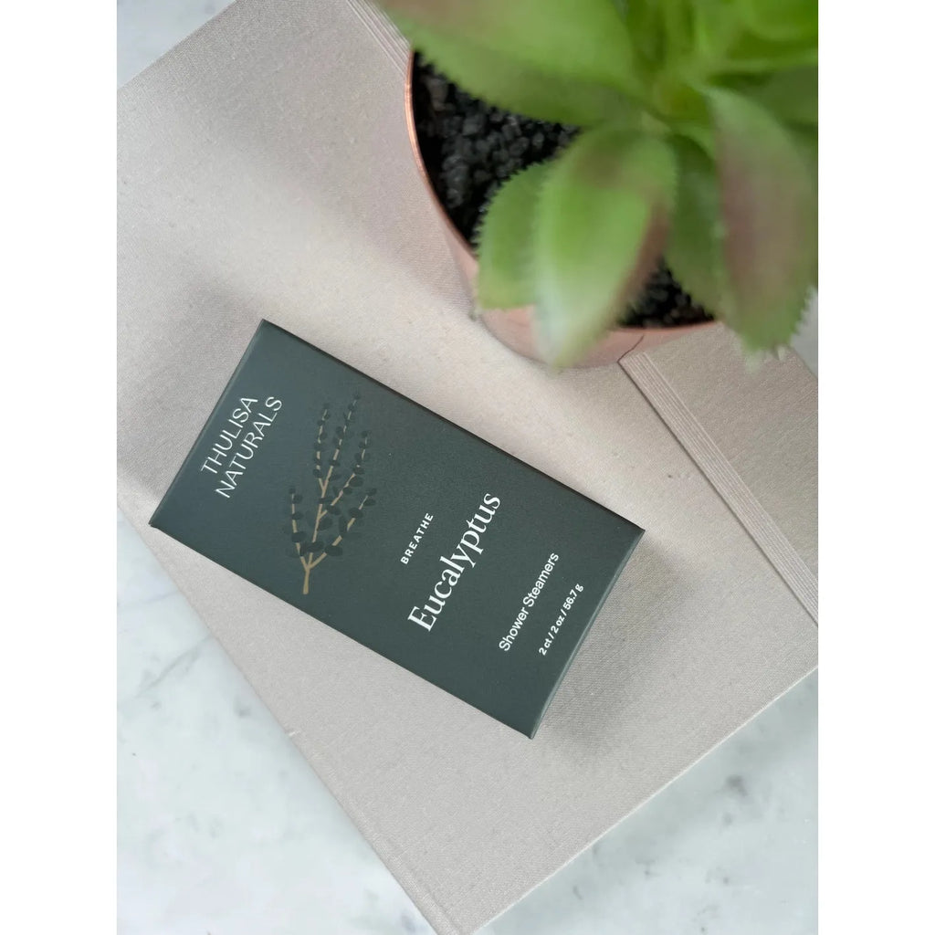 A eucalyptus soap bar packaging resting on a gray fabric surface next to a potted plant.