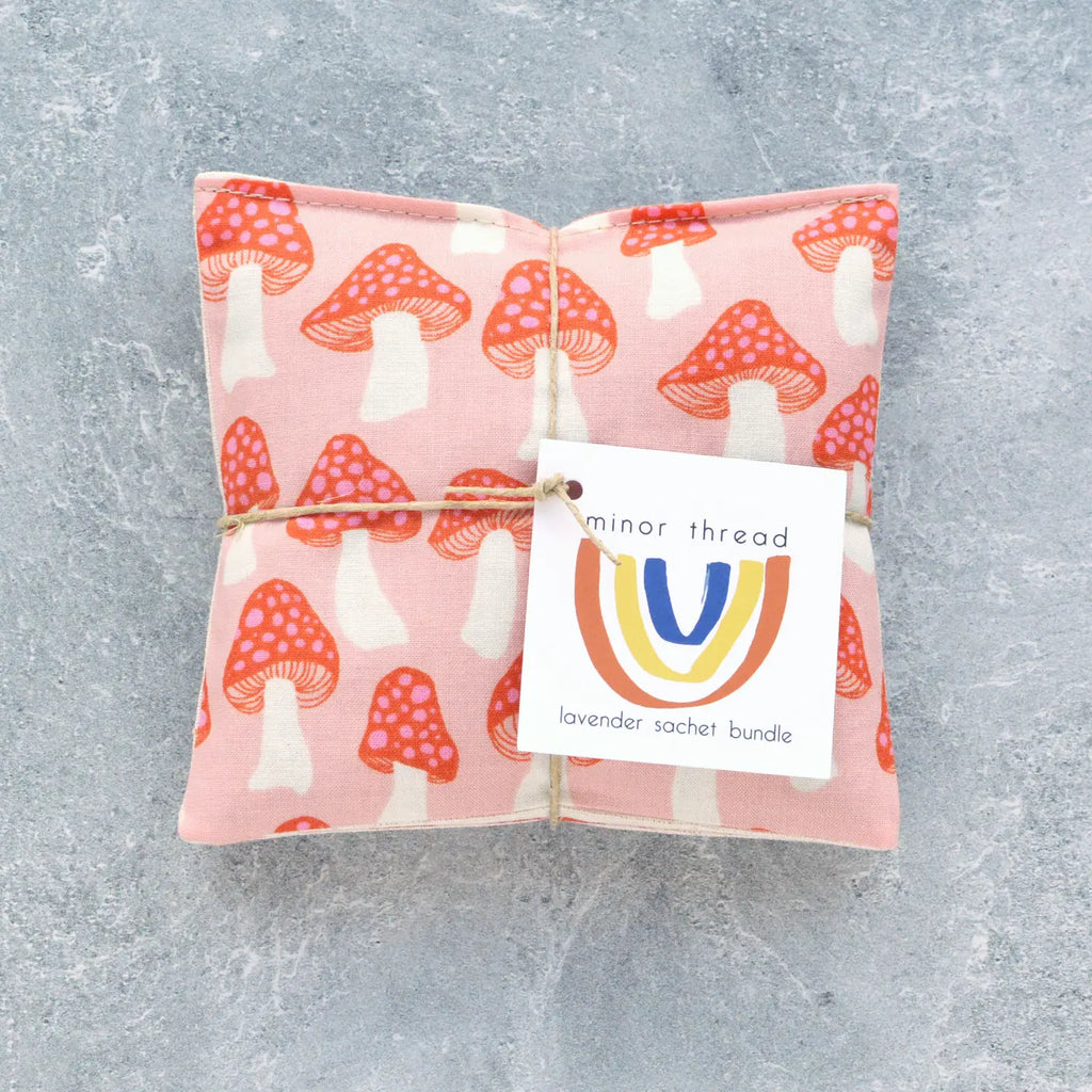 A fabric sachet with a mushroom pattern and a "minor thread" brand label, presented on a textured background.