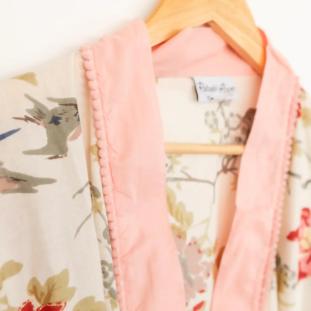A close-up of a floral patterned garment with pink piping on a wooden hanger.