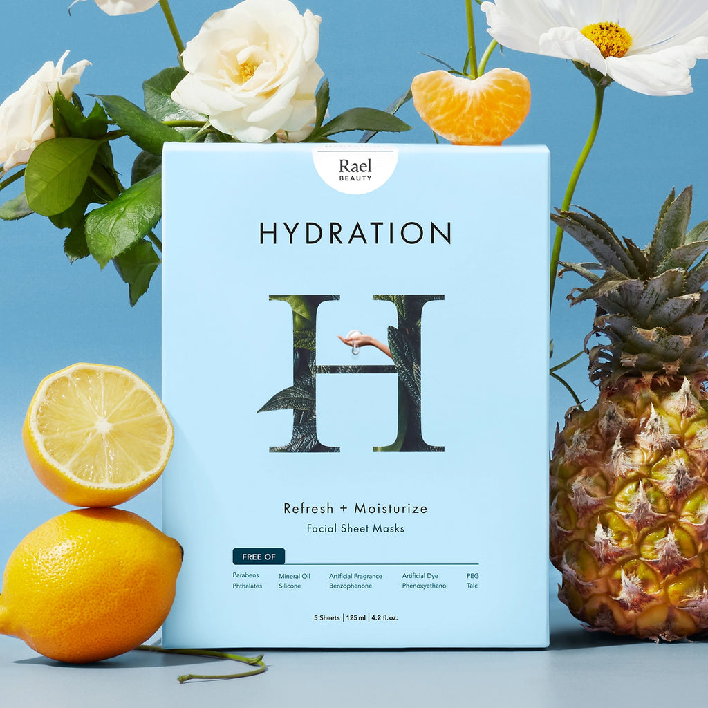 A box of rael beauty hydration facial sheet masks presented with a white rose, lemon, mandarin slice, and a pineapple against a blue background.