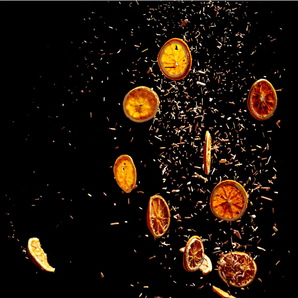 Sliced oranges and scattered spices captured in mid-air against a dark background.