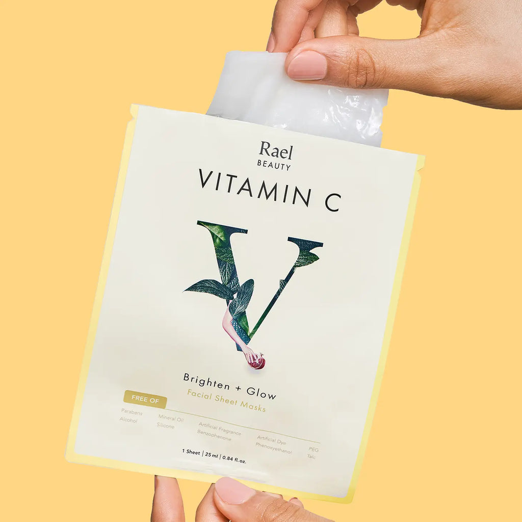 A person holding a rael beauty vitamin c facial sheet mask packaging against a yellow background.