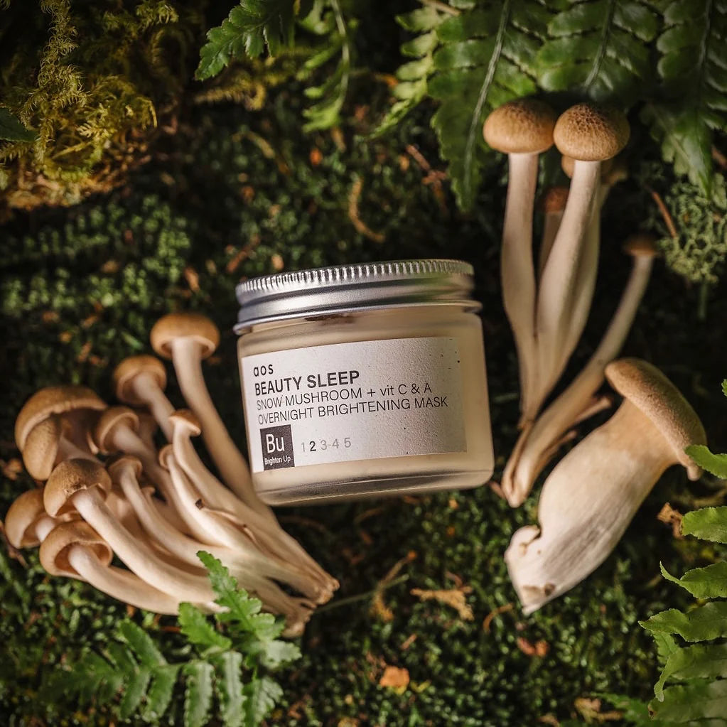 A jar of "beauty sleep" overnight brightening mask surrounded by mushrooms and greenery.