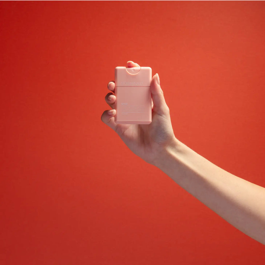 A hand holding a pink perfume bottle against a red background.