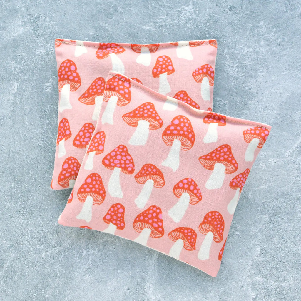 Two fabric pouches with a red and white mushroom pattern on a textured blue background.