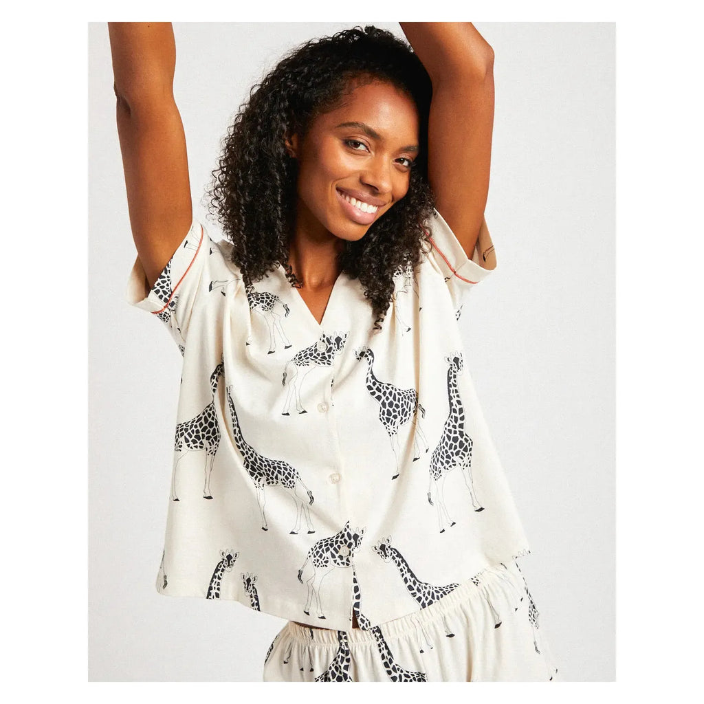 Person smiles and raises their arms while wearing a Chelsea Peers Organic Cotton Giraffe Print two-piece pajama set.