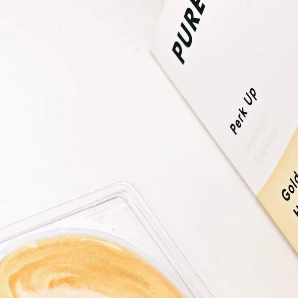 Coffee beside a book titled "pure" with a visible phrase "perk up" on a white surface.