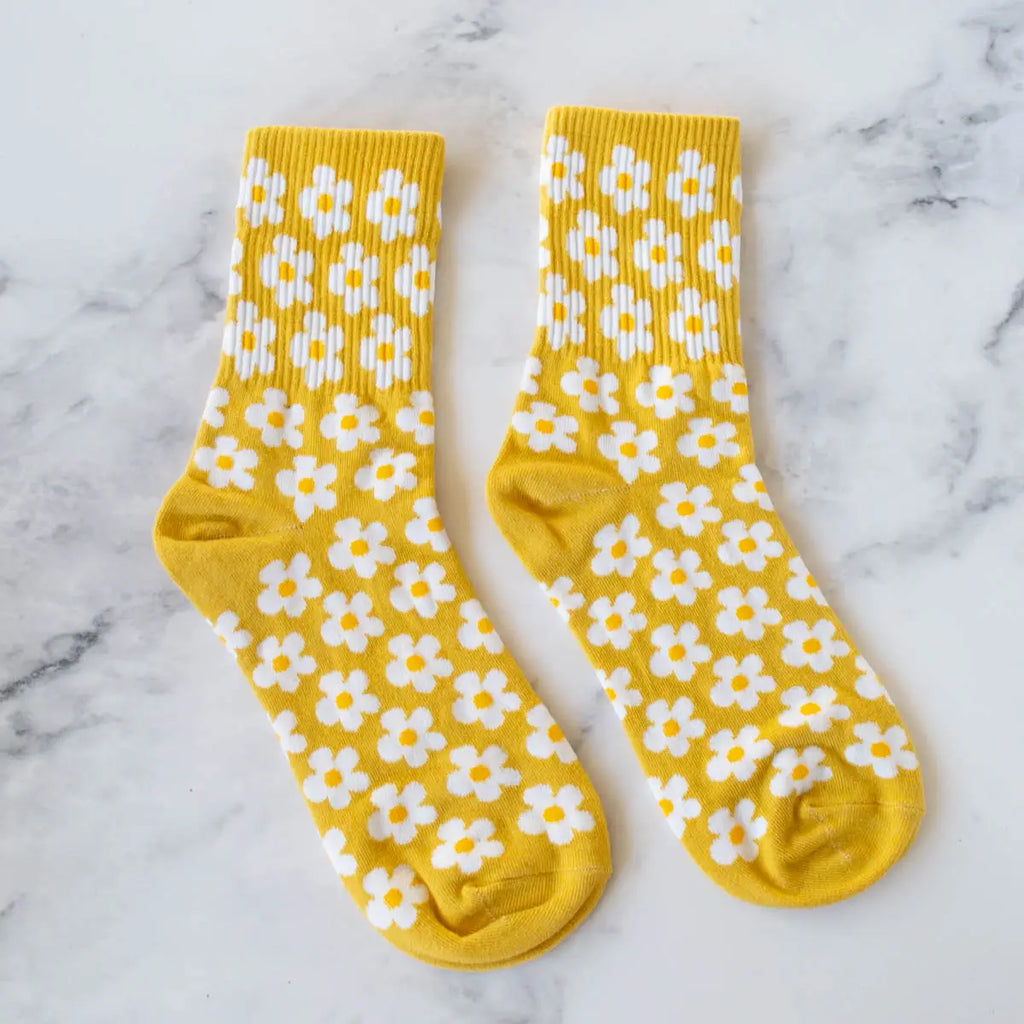A pair of yellow socks with white daisy patterns on a marble surface.