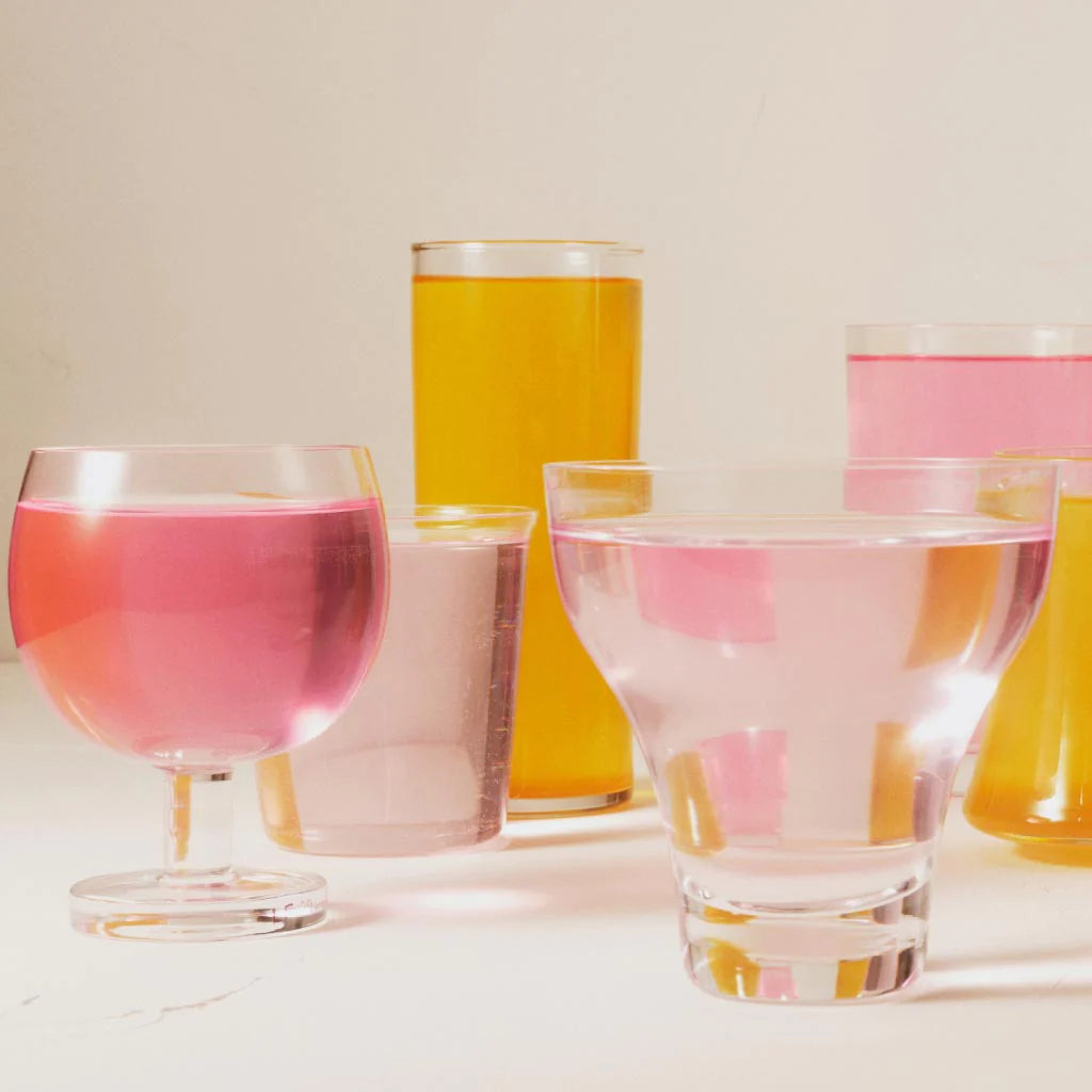 Various glasses containing pink and yellow beverages on a pale surface.