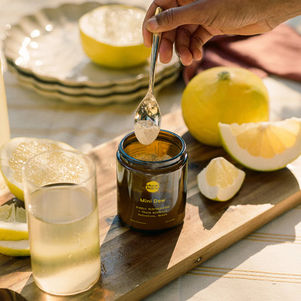 A person spooning honey from a jar amidst cut lemons on a sunny table setting.