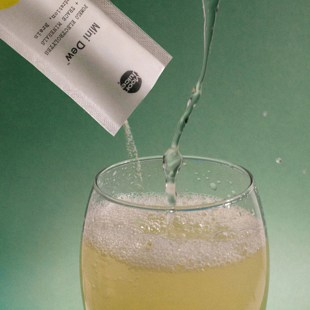 Pouring a clear liquid from a small sachet into a glass of effervescent liquid.