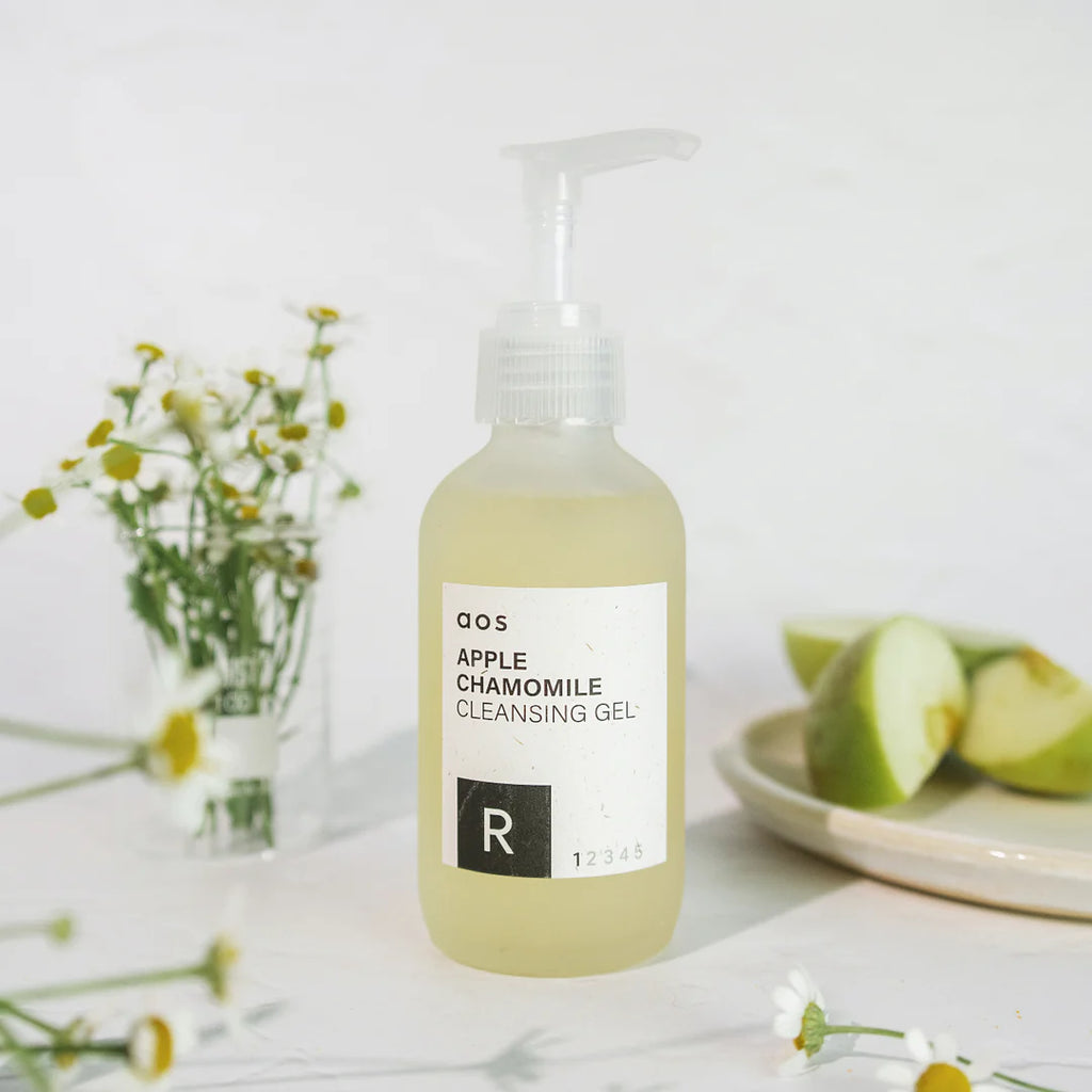 Apple chamomile cleansing gel in a pump bottle with fresh apple slices and chamomile flowers in the background.