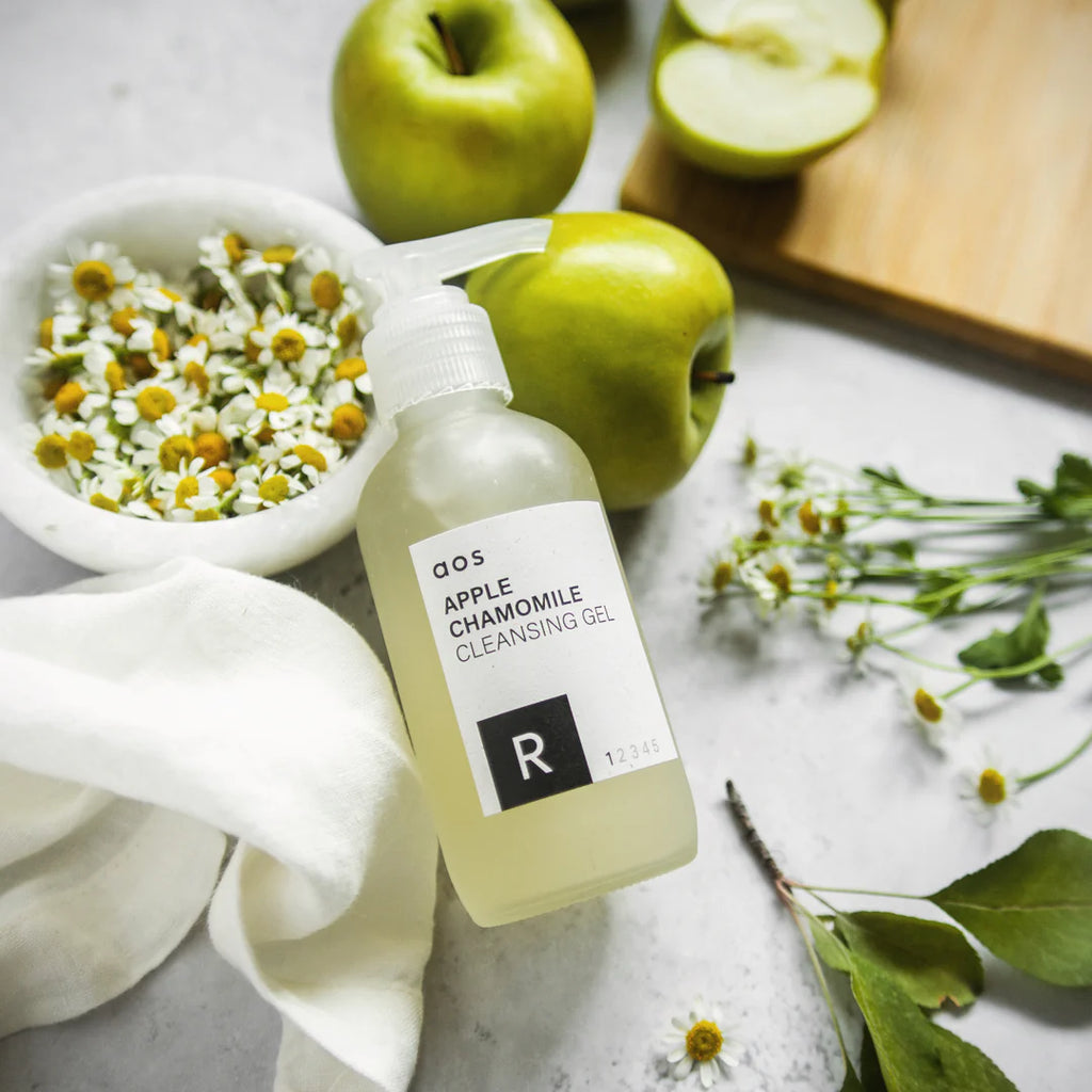 Apple chamomile cleansing gel on a marble surface surrounded by fresh apples and chamomile flowers.