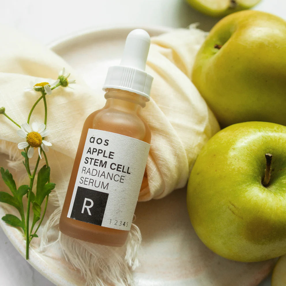 Apple stem cell radiance serum displayed with fresh apples and flowers on a neutral background.
