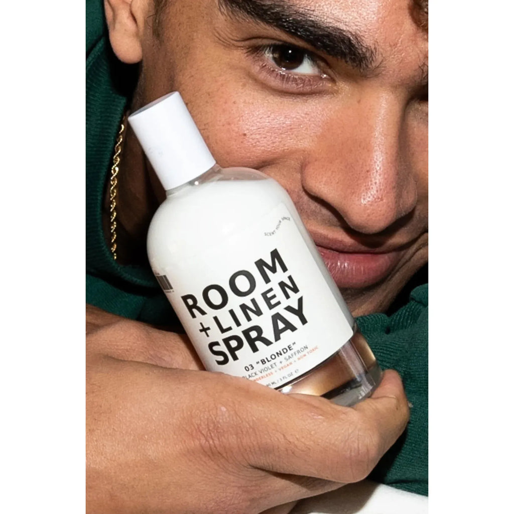 A person holding a bottle of room and linen spray close to their face.