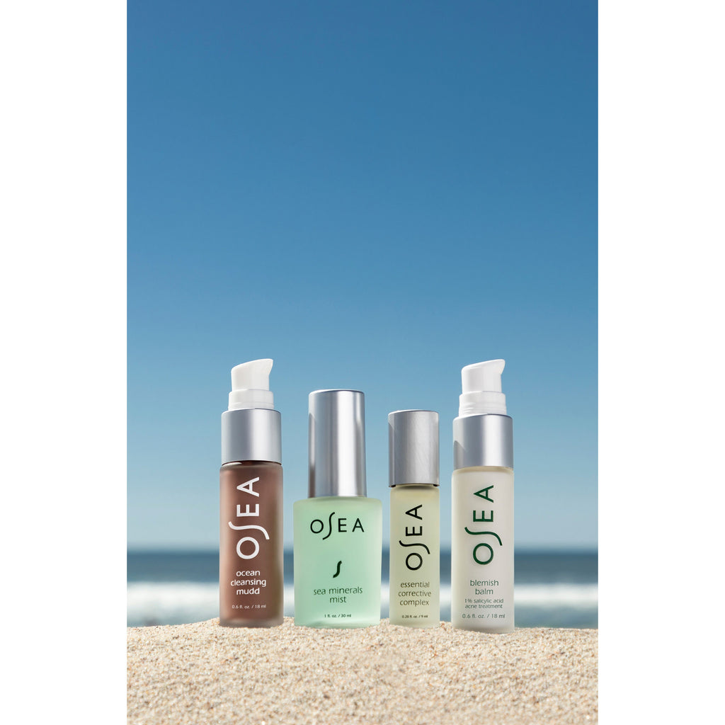 Four skincare products arranged on a sandy beach with a clear blue sky as the backdrop.