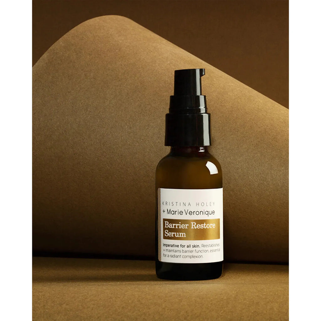A bottle of kristina holey + marie veronique barrier restore serum on a brown background with geometric shadows.