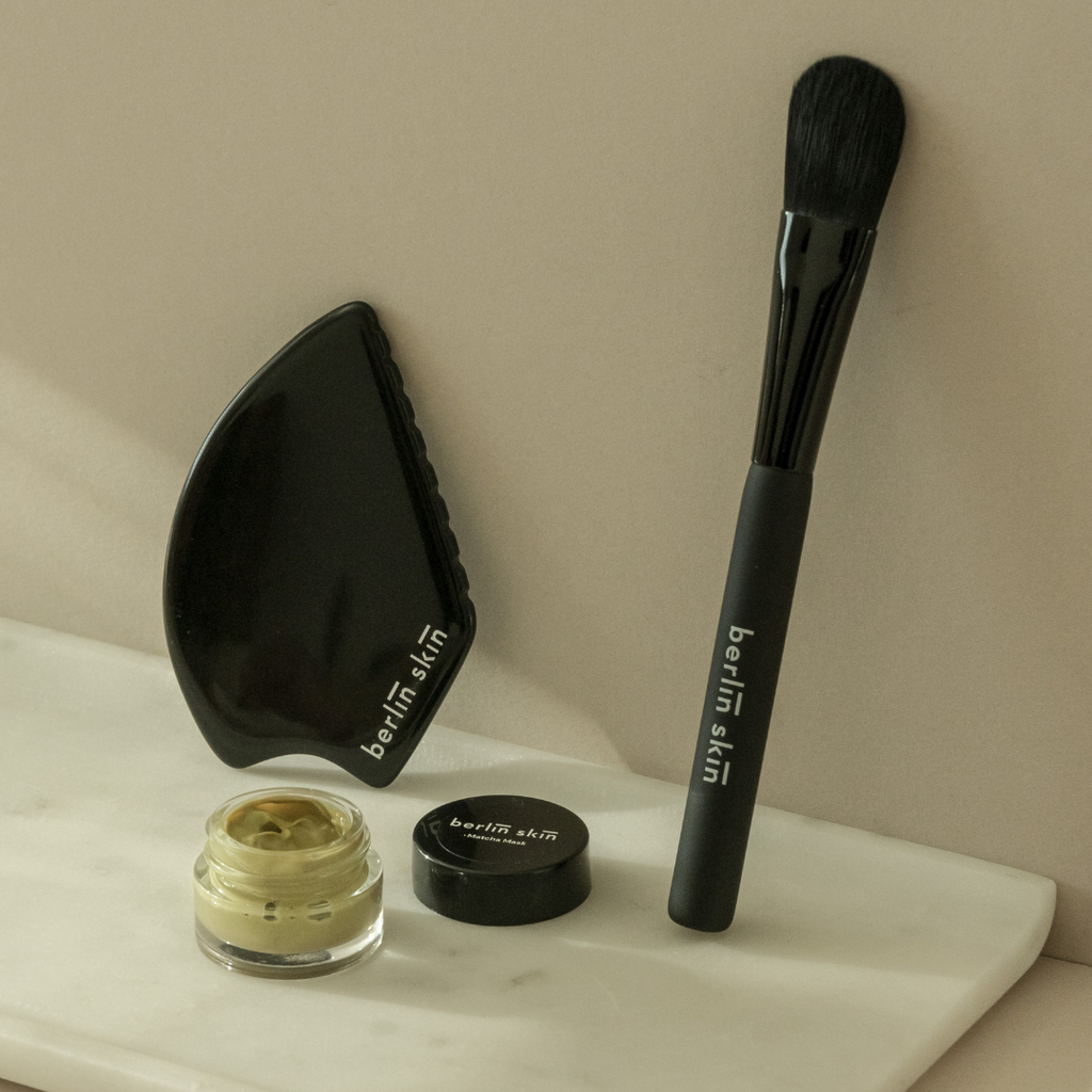 Cosmetic products and a makeup brush displayed on a marble surface.