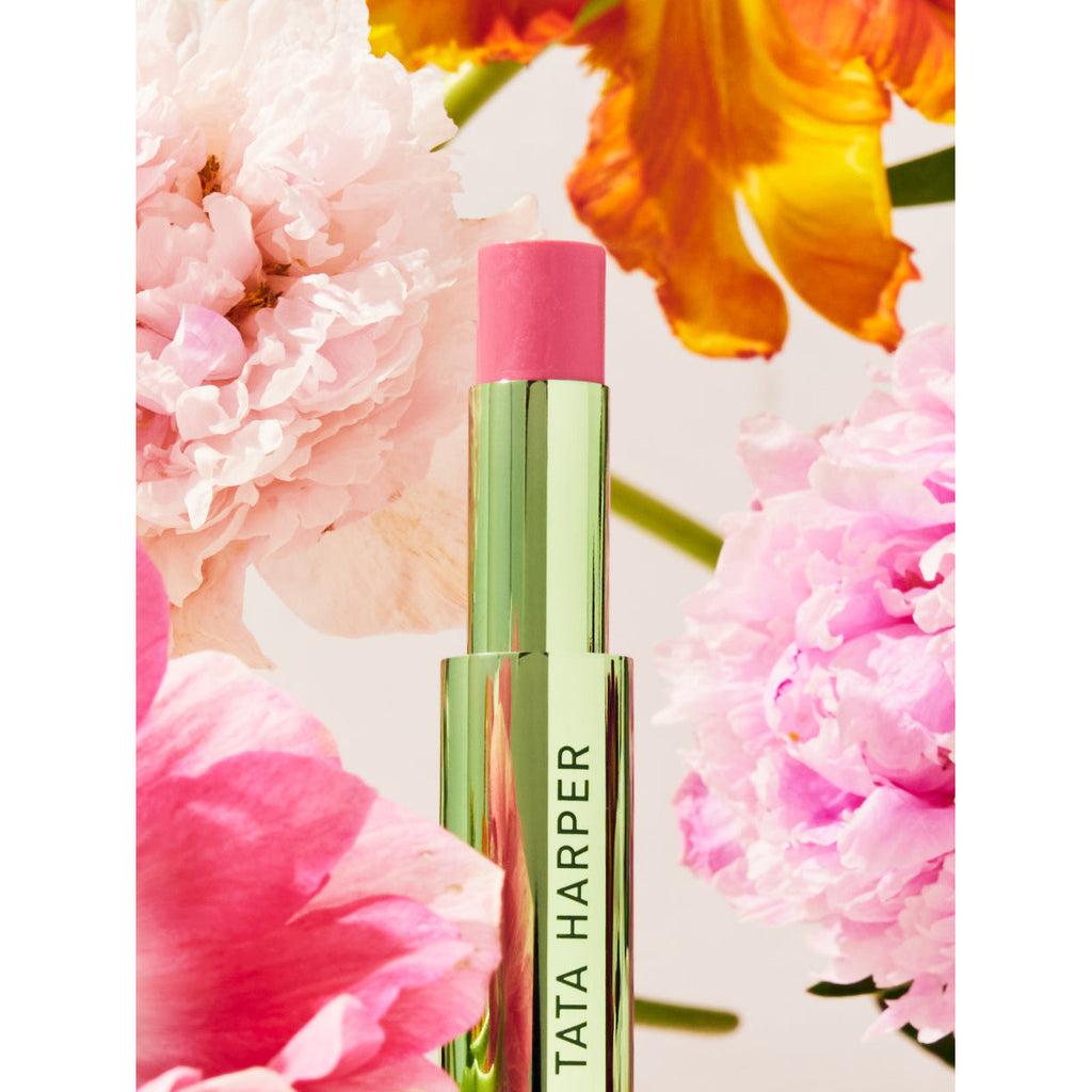A tube of lipstick surrounded by vibrant flowers.