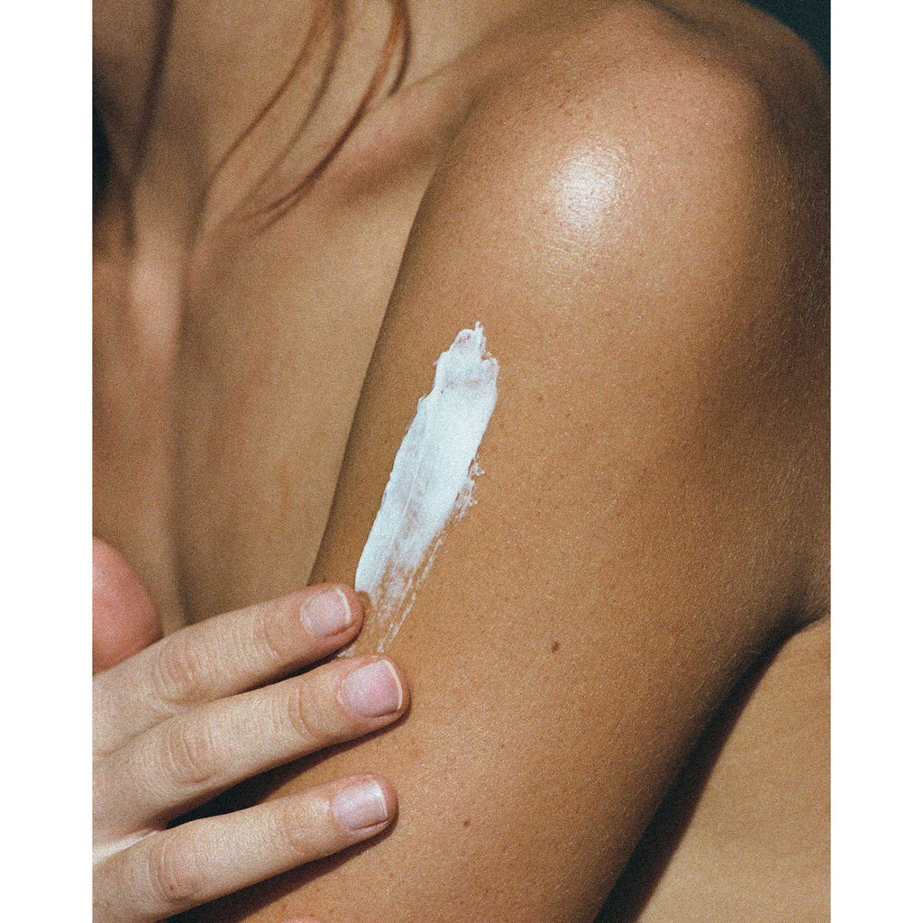 A female model with no top on and a smear of corpus body butter on her upper arm