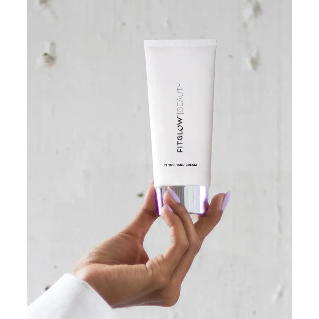 A hand holding a tube of fitglow beauty cloud hand cream against a light background.