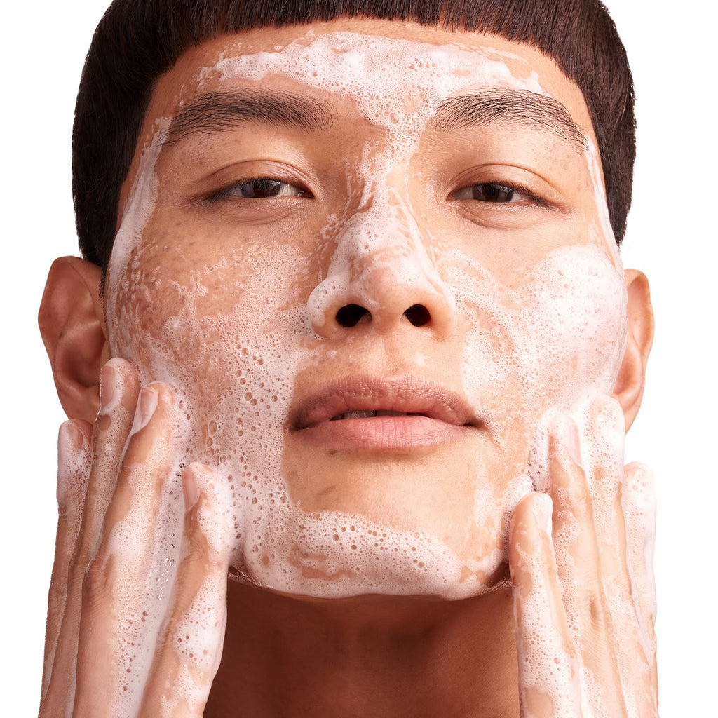 A person applying foamy facial cleanser to their face.