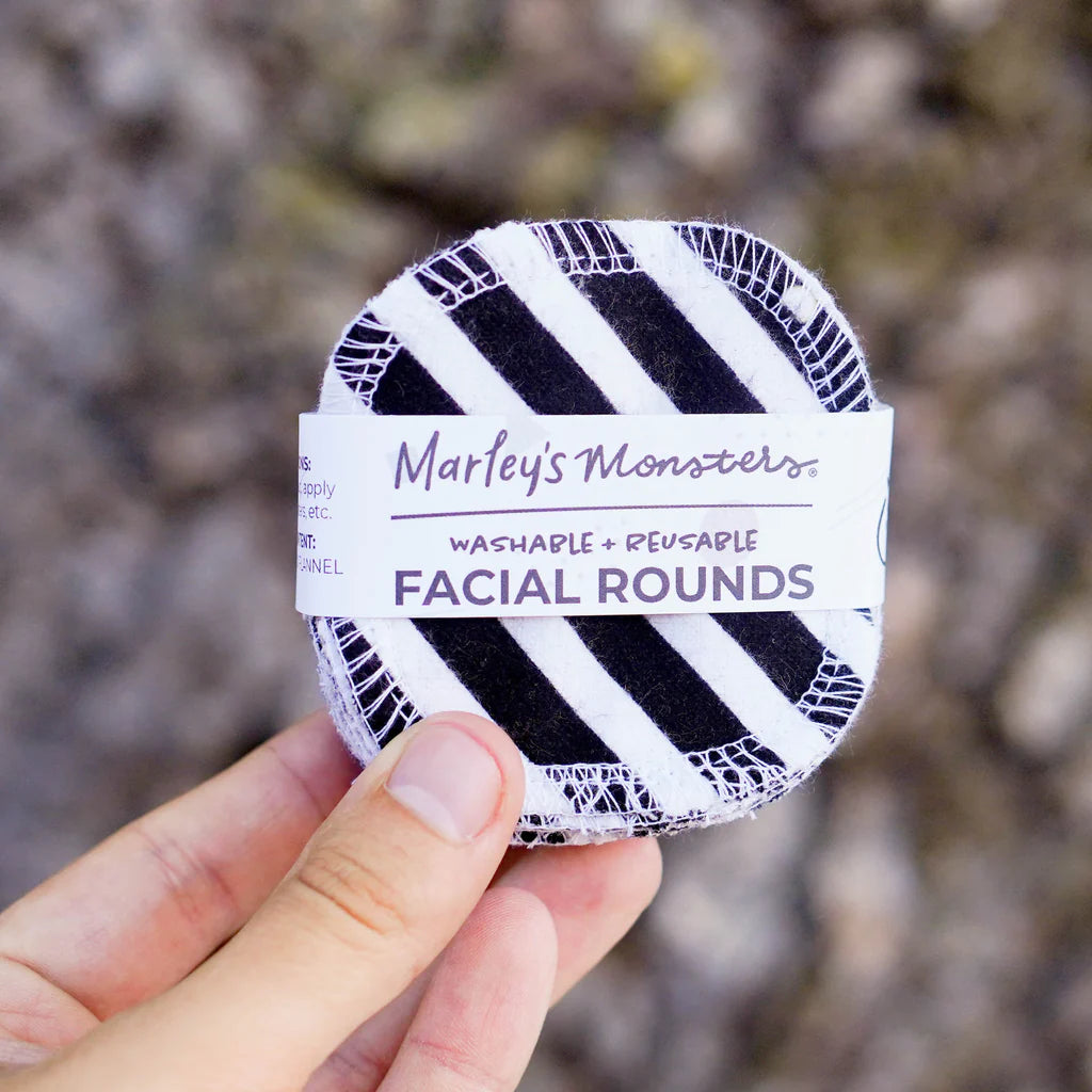 A hand holding a washable and reusable facial round with a black and white striped pattern from marley's monsters.