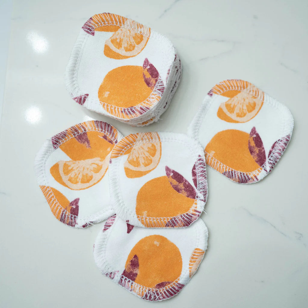 Five cloth pads with orange fruit patterns on a marble surface.
