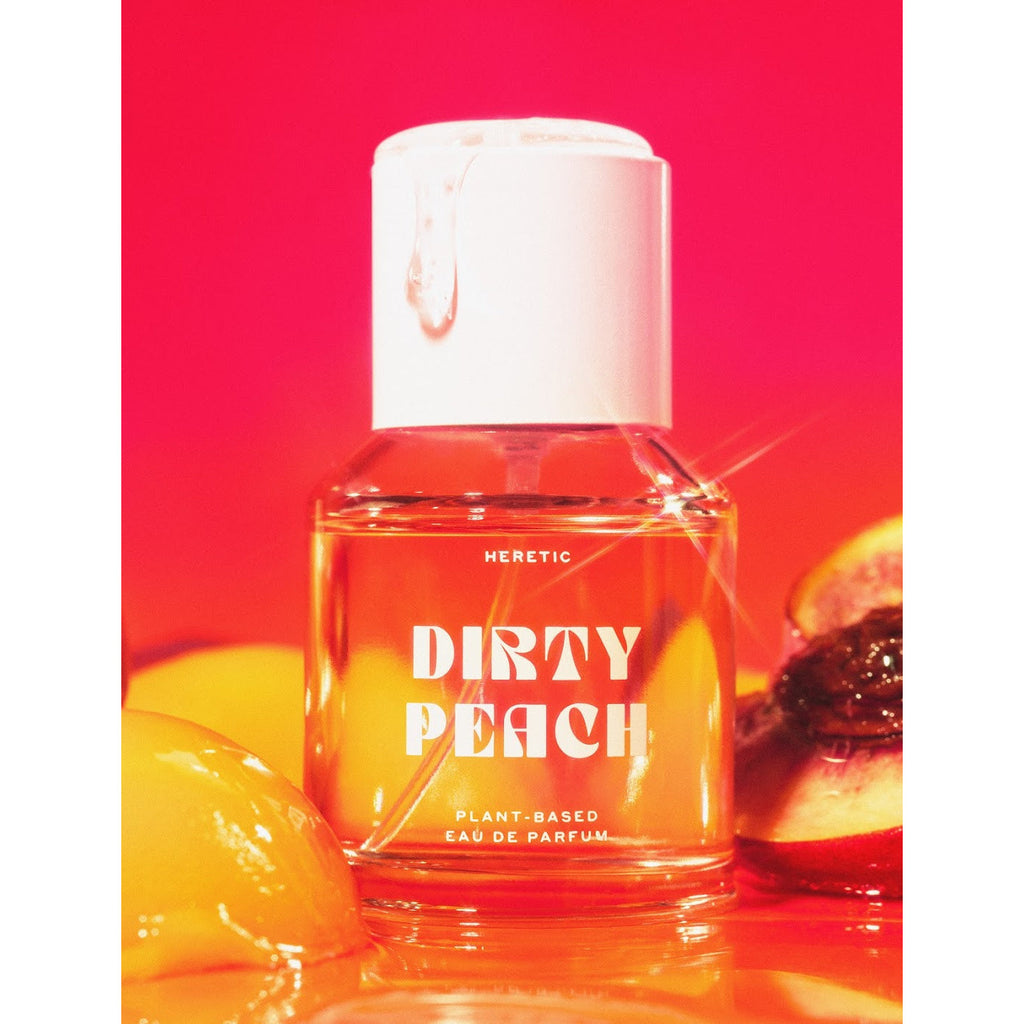 A bottle of heretic dirty peach plant-based perfume displayed against a red background, accompanied by peach and lemon slices.