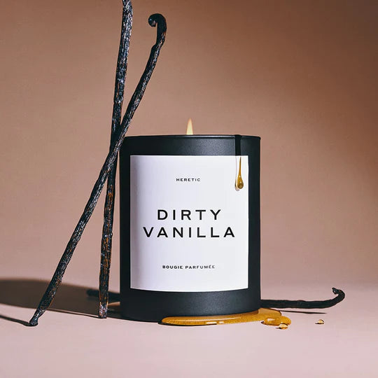 A lit "dirty vanilla" scented candle with a black container and vanilla pods in the background.