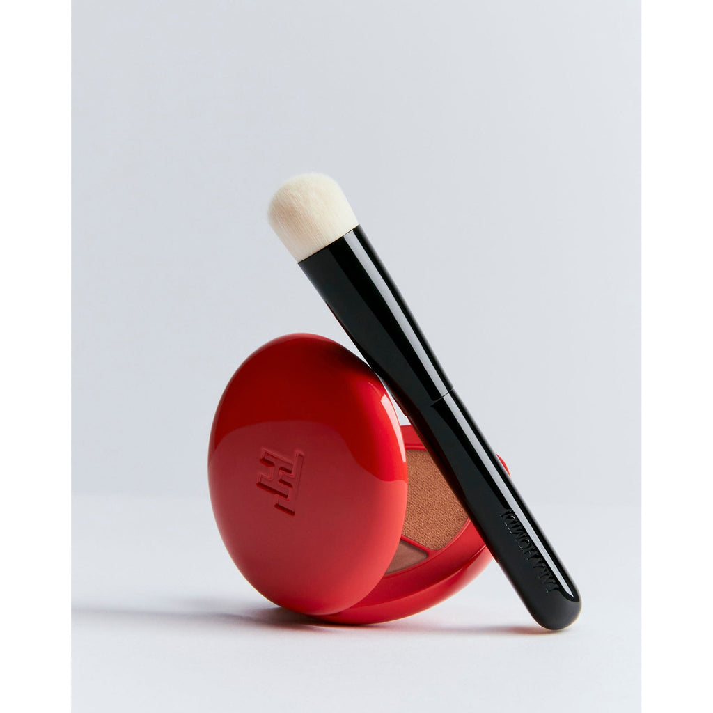 A makeup brush resting on a compact blush with a red case.