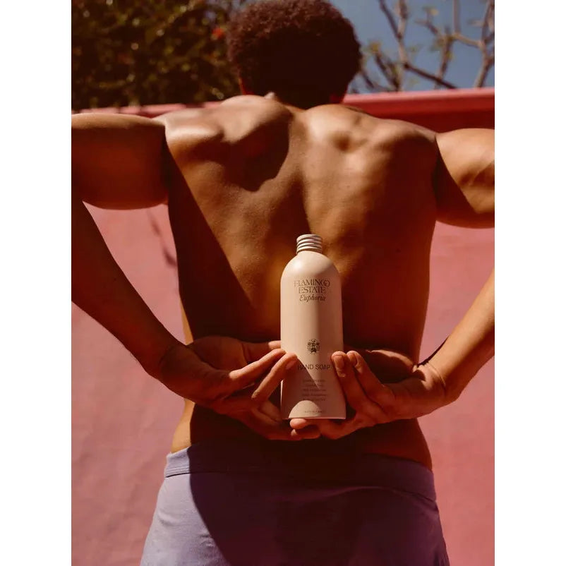 A person holding a bottle of sunscreen on their lower back, preparing to apply it, under sunny conditions.