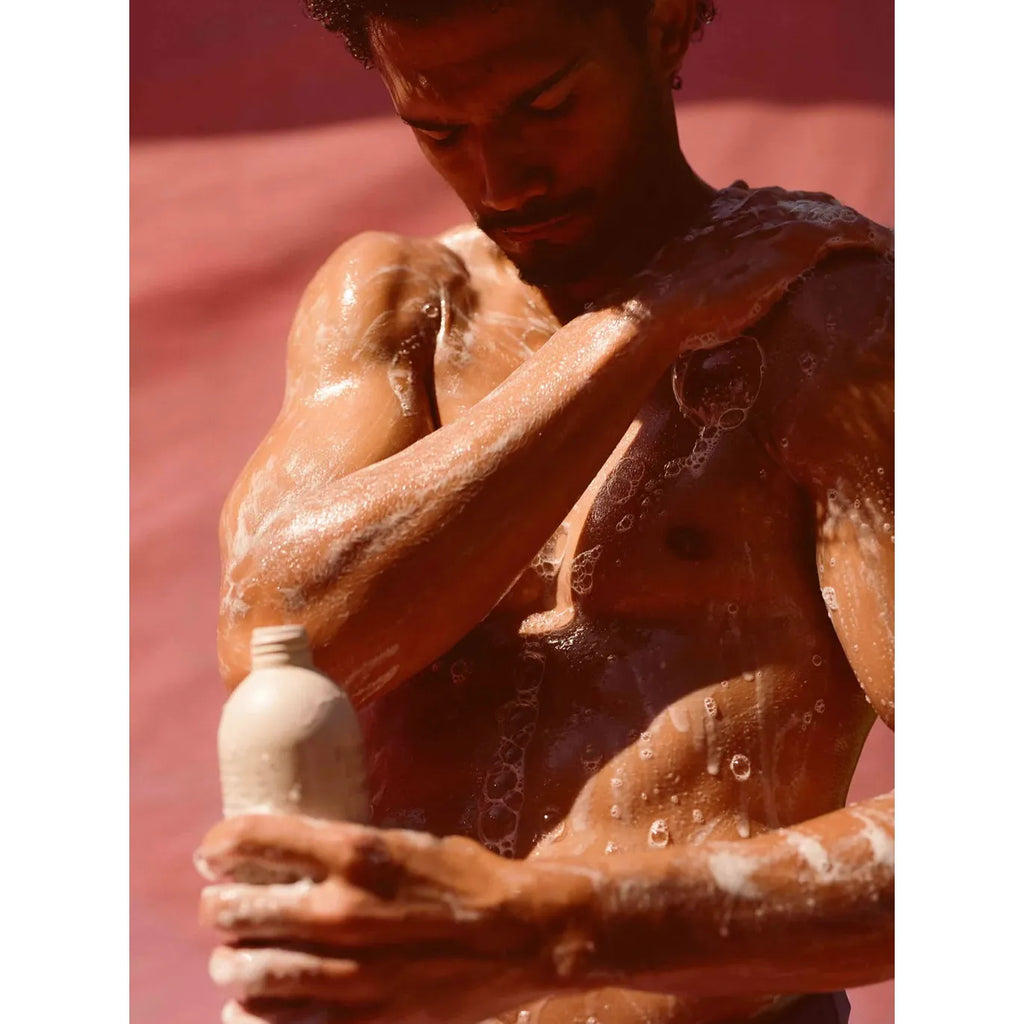 A person showering outdoors, applying body wash or lotion.