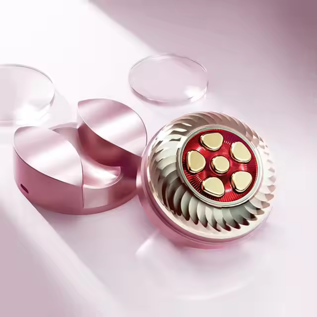 Close-up of the Wren and Wild RF/LED Facial Tool, showcasing a circular, gear-like design with red and gold accents. It's surrounded by reflective surfaces on a soft pink background.