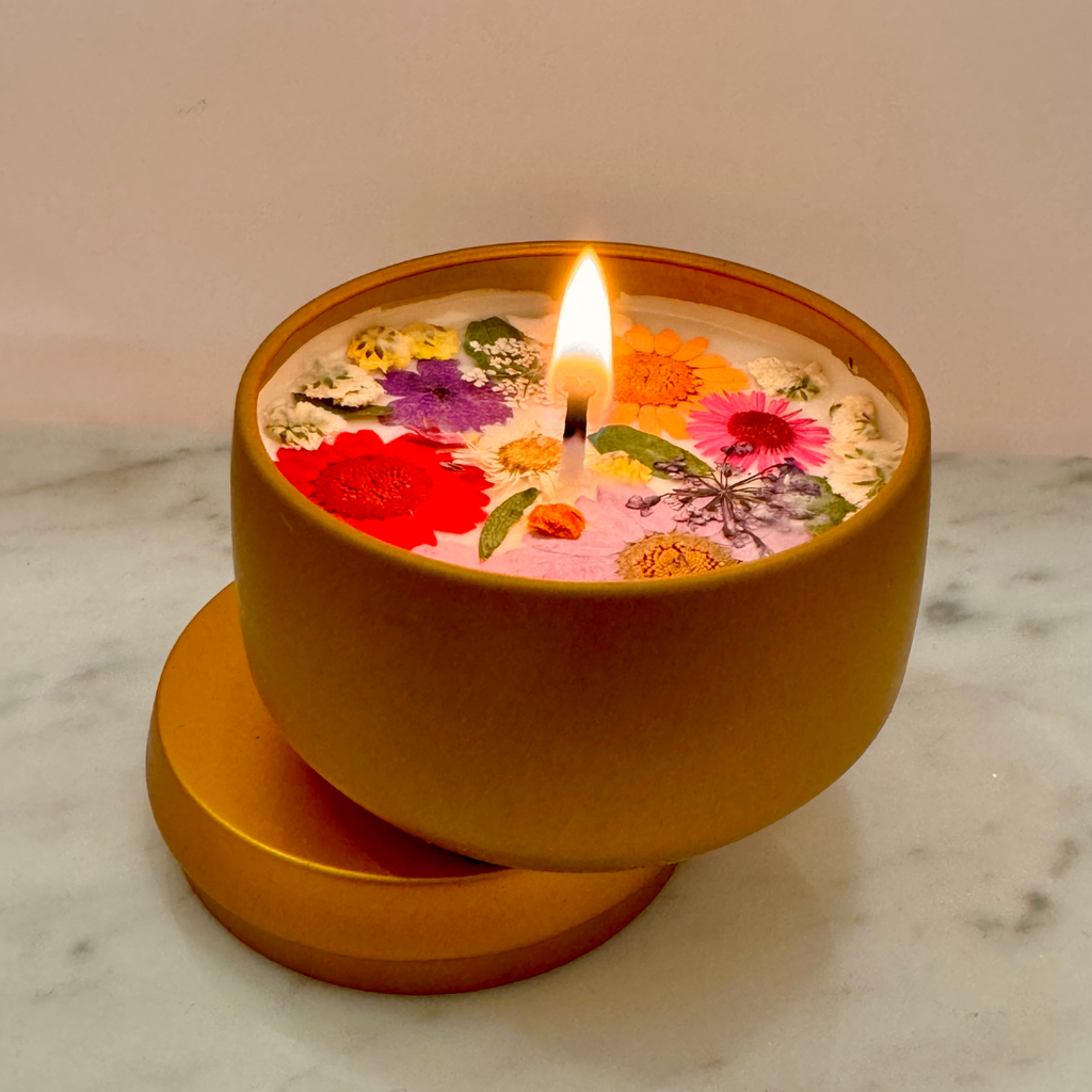 The Goodbye Summer Candle, made from natural plant-based wax and essential oils, is beautifully housed in a gold container with embedded dried flowers, resting on a marble surface.