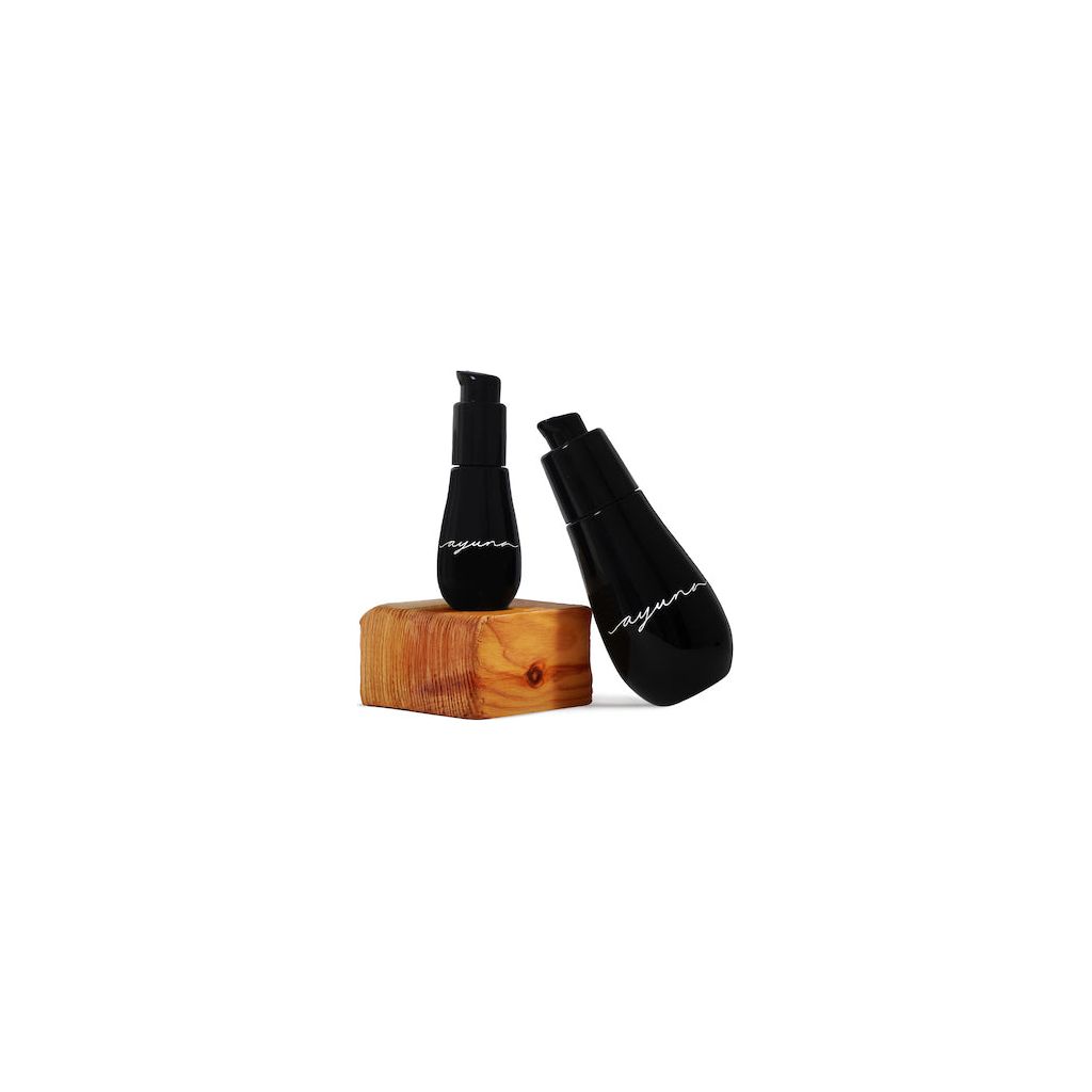 Two Ayuna cosmetic bottles with black labels placed beside a block of wood on a white background.