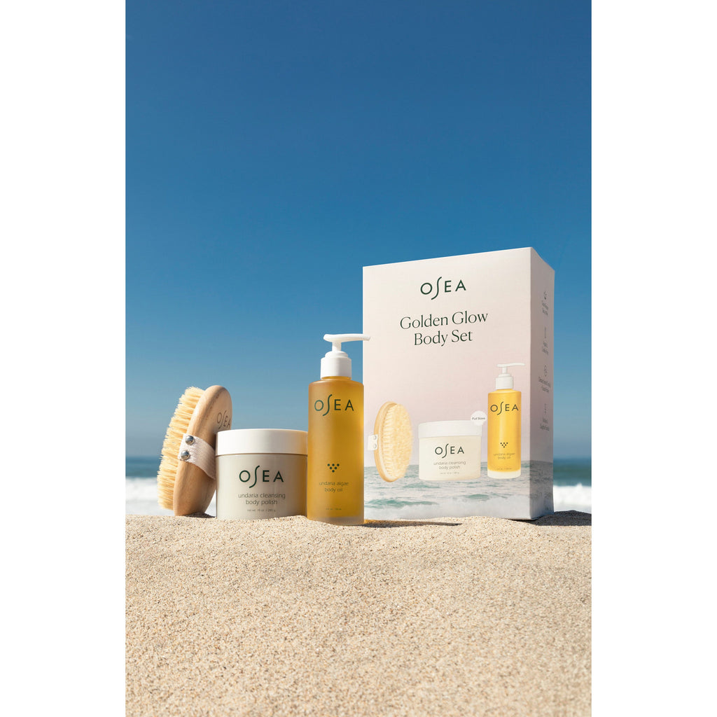A collection of osea skincare products arranged on a sandy beach with a clear blue sky in the background.