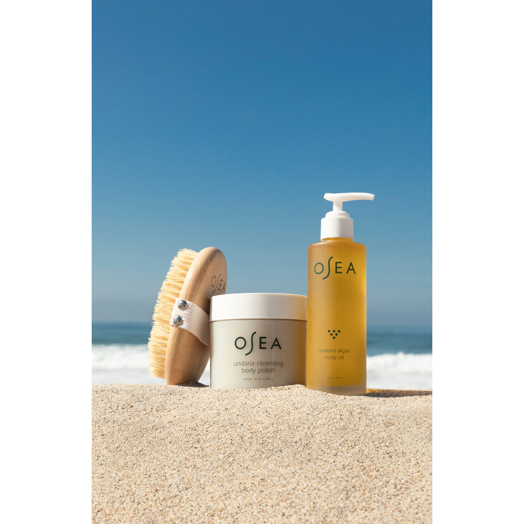 Skincare products and a brush on a sandy beach with clear blue sky in the background.