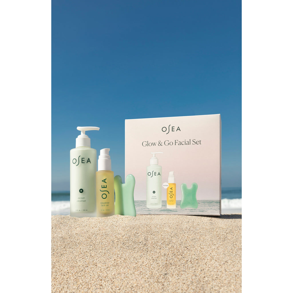 A set of cosmetic products by osea displayed on sandy beach with clear blue sky in the background.