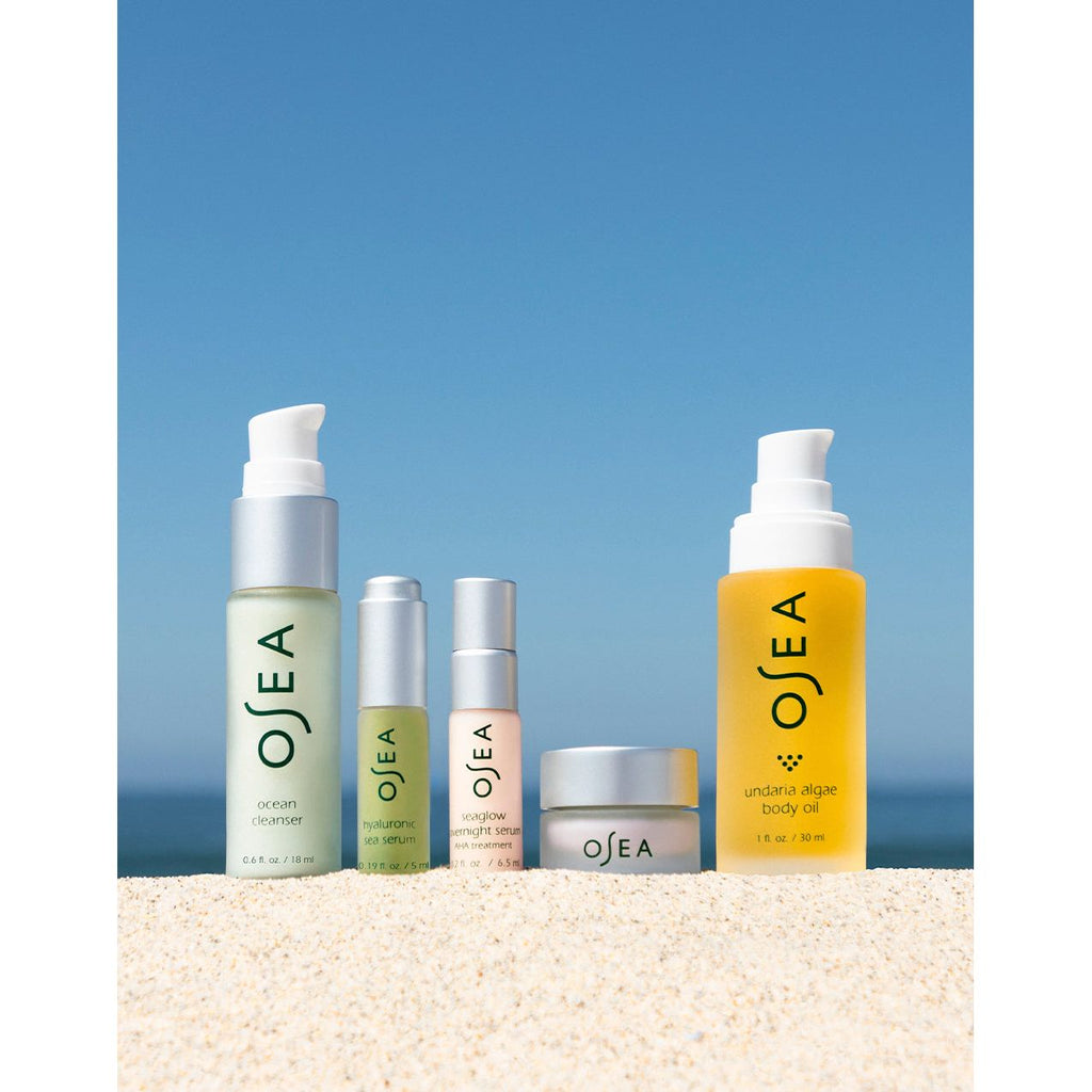 A set of skincare products arranged on sandy beach with a clear blue sky in the background.