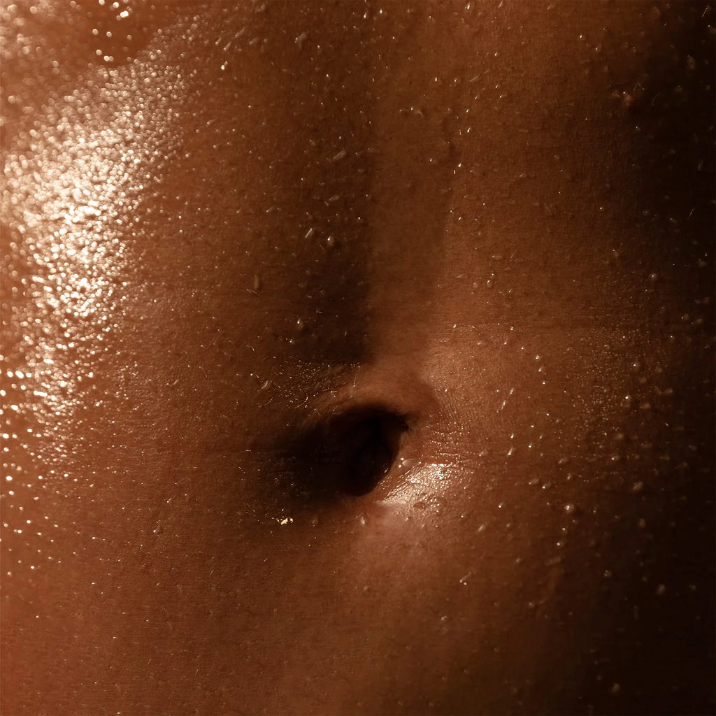 Close-up of a human navel on skin with moisture droplets.