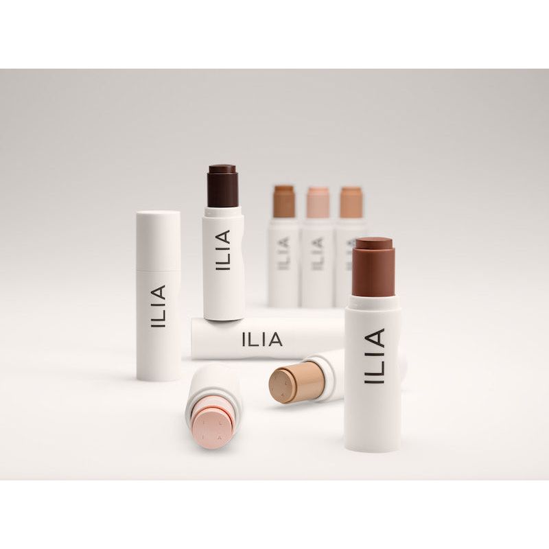 A collection of ilia-branded cosmetic products with neutral-toned packaging, displayed against a light background.